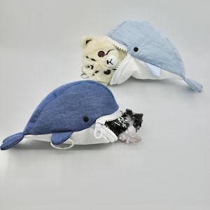 May include: Two plush whale-shaped zippered pouches. One is blue denim with a white lining and a silver key ring. The other is light blue with a white lining and a brown bear peeking out of the zippered opening.