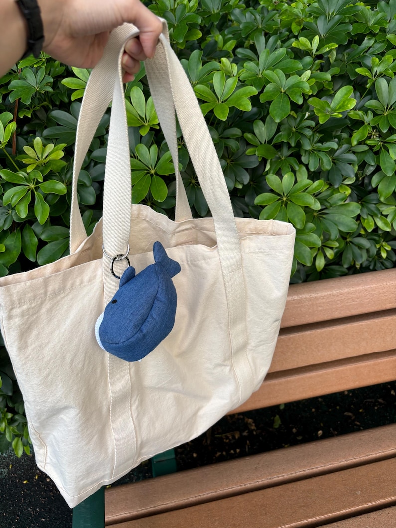 May include: A cream-coloured canvas tote bag with a blue whale plush keychain attached to the handle.