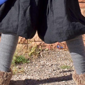 May include: A pair of black, loose-fitting pants with a gathered waist and a gray pair of leggings underneath. The pants are worn by a person standing on a dirt path with brown rocks and green plants.