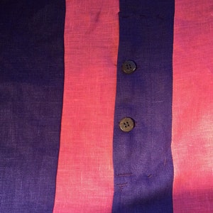 May include: A close-up of a striped fabric with two buttons. The fabric is a combination of pink and purple stripes.