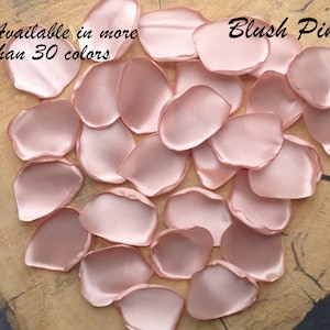 May include: Blush pink satin rose petals, available in over 30 colors. The petals are scattered on a wooden surface.
