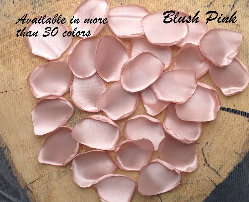 May include: Blush pink satin rose petals, available in over 30 colors. The petals are scattered on a wooden surface.