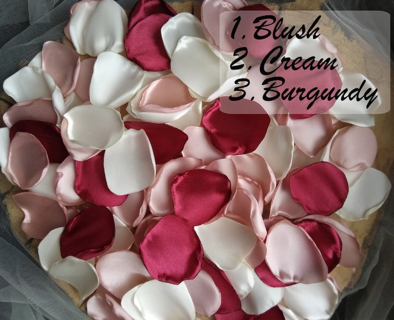 May include: A pile of silk rose petals in blush, cream, and burgundy colors. The petals are arranged in a heart shape. 1. Blush 2. Cream 3. Burgundy