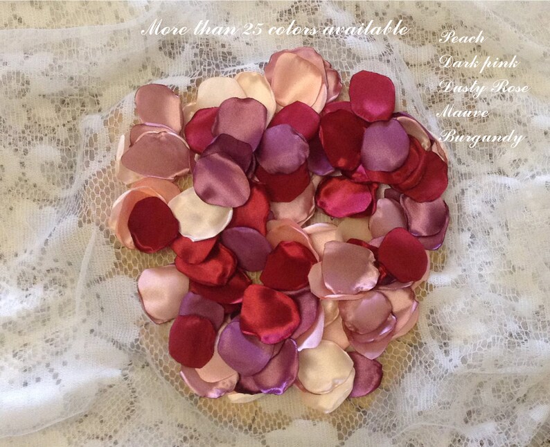May include: A collection of satin rose petals in various shades of pink, red, and purple. The petals are arranged in a heart shape on a white lace background. The text "More than 25 colors available" is visible at the top of the image. The text "Peach, Dark pink, Dusty Rose, Mauve, Burgundy" is visible on the right side of the image.