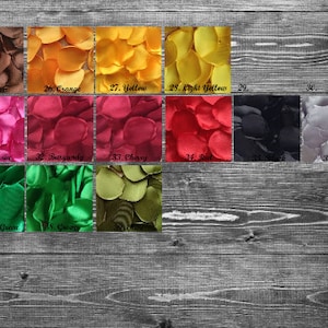 May include: Assortment of silk rose petals in various colors, including brown, orange, yellow, fuchsia, burgundy, cherry, red, black, and gray. The petals are arranged in rows on a wooden surface.