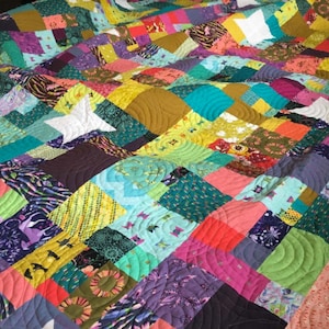 May include: A colorful patchwork quilt with a variety of fabrics and patterns. The quilt is quilted with a wavy design.