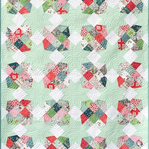 May include: A quilt with a green background and a white diamond pattern. The quilt is made up of smaller squares of fabric in various shades of pink, red, and green. The quilt is quilted with a swirling pattern.