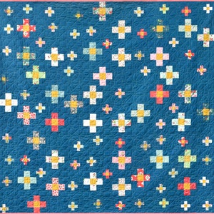 May include: A blue quilt with a pink border and a pattern of white and red plus signs. The plus signs are arranged in a random pattern.
