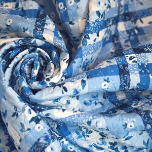 May include: A blue and white patchwork quilt with a floral pattern. The quilt is folded in a spiral shape.