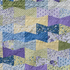 Op de afbeelding: Close-up van een patchwork quilt met een verscheidenheid aan patronen en kleuren. De quilt heeft geometrische vormen in tinten blauw, groen, geel en paars. De quiltsteken voegen textuur en detail toe aan de stof.