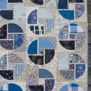 Może przedstawiać: Kołdra z geometrycznym wzorem niebieskich i białych kół. Koła są wykonane z mniejszych kawałków tkaniny w różnych wzorach i kolorach. Kołdra jest pikowana białą nicią.