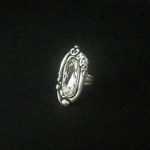 May include: A silver ring with an oval-shaped clear crystal set in a detailed design.