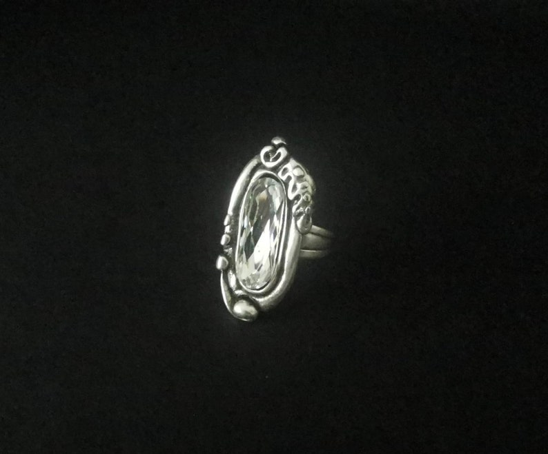 May include: A silver ring with an oval-shaped clear crystal set in a detailed design.