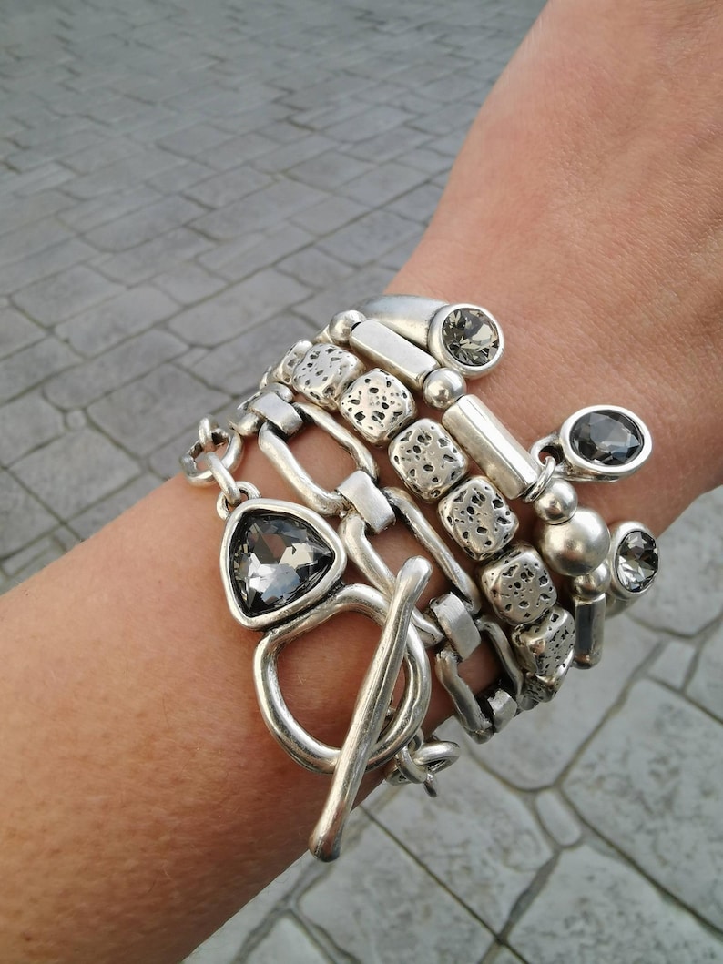 Stack of five silver plated bracelets on a wrist featuring smoky grey crystals, toggle clasp and textured beads.