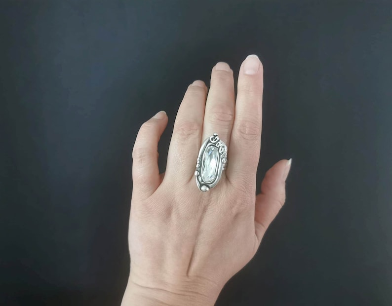 A silver plated ring with an oval-shaped clear crystal set in a decorative silver setting.