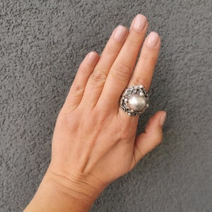 Peut inclure: Une bague en argent avec une grosse pierre centrale ronde et texturée. La bague est portée au doigt.