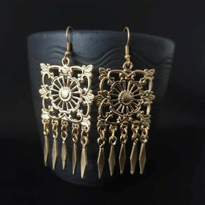 Può includere: Orecchini pendenti dorati con un designo quadrato ornato e una frangia di catene e ciondoli a forma di lacrima.