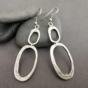 May include: A pair of silver dangle earrings with a textured finish. Each earring features two connected oval shapes.