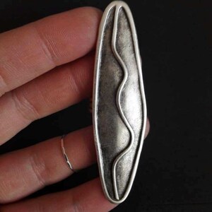 May include: A silver-toned pendant with a wavy line design inside a rounded oval shape.