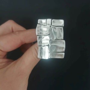 May include: A silver ring with a textured design resembling stacked stones.