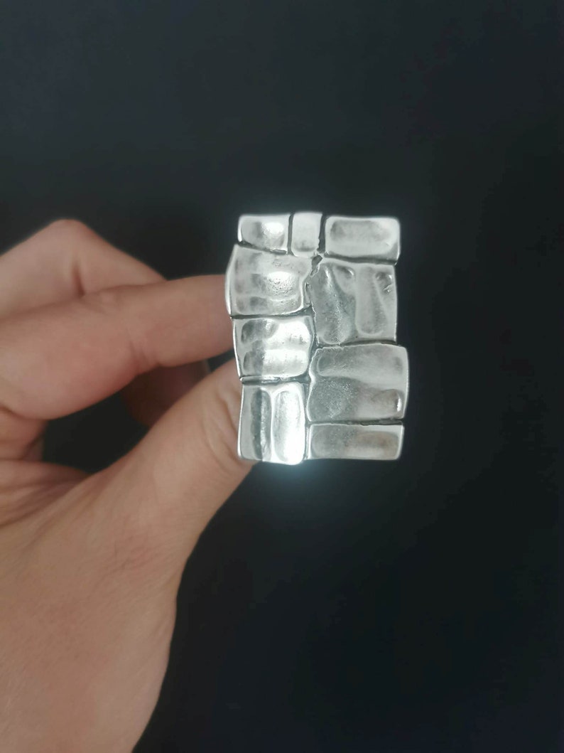 May include: A silver ring with a textured design resembling stacked stones.