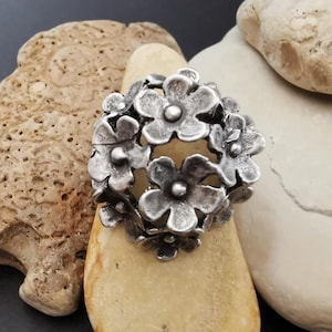 Könnte beinhalten: Ein silberner Anhänger in Form eines Blumenstraußes. Die Blumen sind detailliert und haben eine strukturierte Oberfläche.