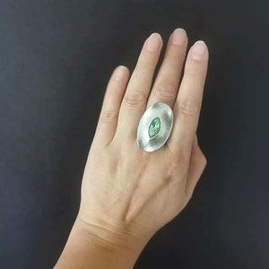 Puede incluir: Un anillo de plata con una gran piedra preciosa ovalada verde engastada en el centro.
