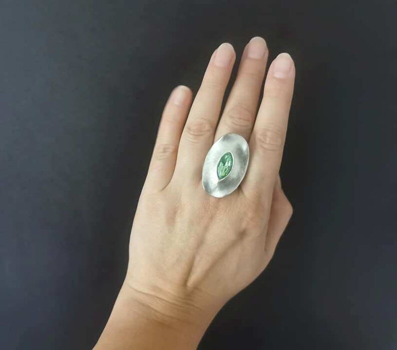 Puede incluir: Un anillo de plata con una gran piedra preciosa ovalada verde engastada en el centro.