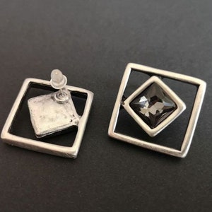 May include: A pair of silver tone earrings with a square design. Each earring features a black square-shaped gemstone set in a silver frame.