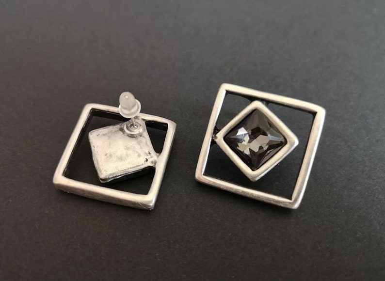 May include: A pair of silver tone earrings with a square design. Each earring features a black square-shaped gemstone set in a silver frame.