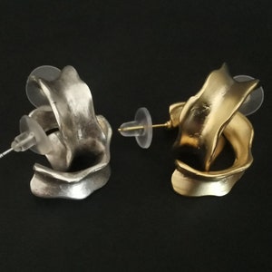 May include: A pair of earrings with a unique, abstract design. One earring is silver and the other is gold.