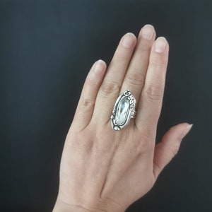 May include: A silver ring with a large clear oval-shaped stone set in a detailed design.