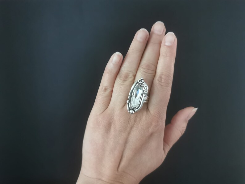 May include: A silver ring with a large clear oval-shaped stone set in a detailed design.