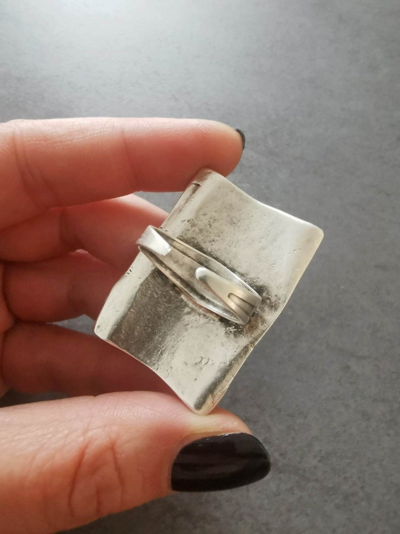 May include: A silver-toned, rectangular, hinged box with a textured surface. The box is closed and has a clasp on the top.