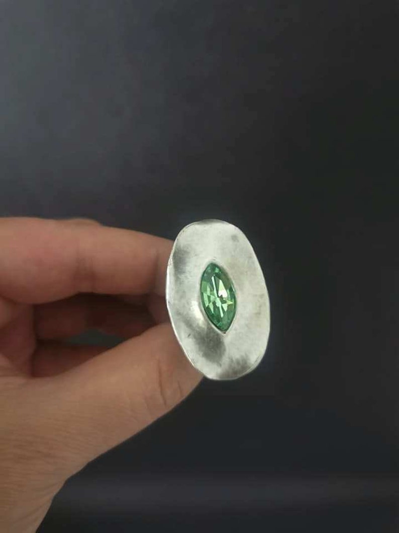 Puede incluir: Un anillo de plata con una piedra preciosa verde engastada en el centro. El anillo tiene forma ovalada y una superficie texturizada.