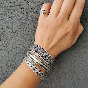 Può includere: Un set di quattro braccialetti d'argento con disegni intrecciati. I braccialetti sono impilati sul polso di una persona.