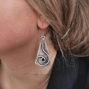 May include: Silver dangle earrings with a geometric triangle shape and a swirl design.