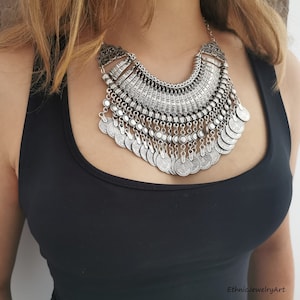 May include: A silver statement necklace with a large, ornate pendant and multiple layers of coin-shaped charms.