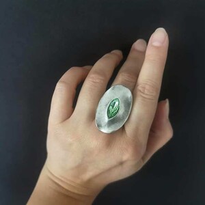 Puede incluir: Un anillo de plata con una piedra preciosa verde engastada en forma ovalada.