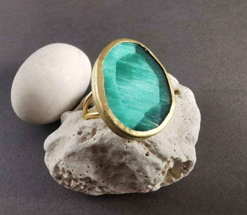 Peut inclure: Bague dor&eacute;e orn&eacute;e d'une grande pierre verte ovale et facett&eacute;e. La pierre est sertie dans un cadre dor&eacute; et repose sur une pierre textur&eacute;e blanc cass&eacute;. Le chaton de la bague est &eacute;galement dor&eacute;.