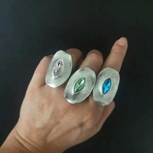 Puede incluir: Tres anillos de plata con engastes ovalados. Cada anillo presenta una gema de color diferente: rosa, verde y azul.
