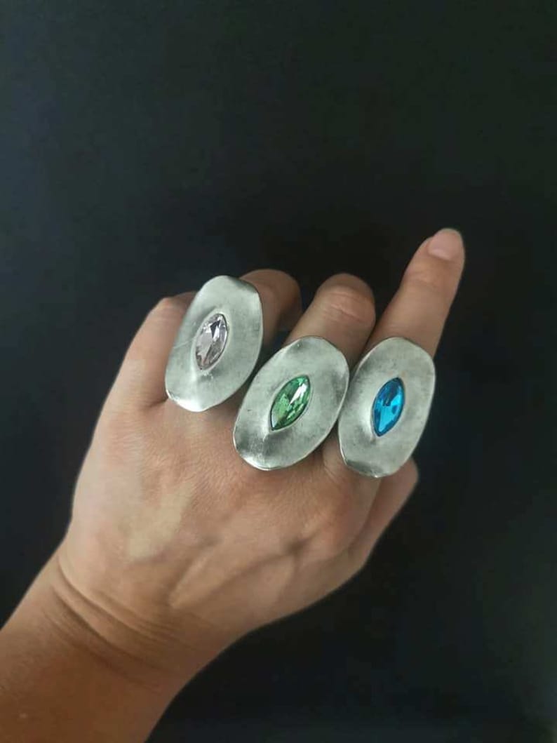 Puede incluir: Tres anillos de plata con engastes ovalados. Cada anillo presenta una gema de color diferente: rosa, verde y azul.