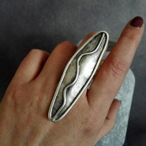 May include: A silver ring with a wavy design. The ring is oval shaped and has a textured finish.