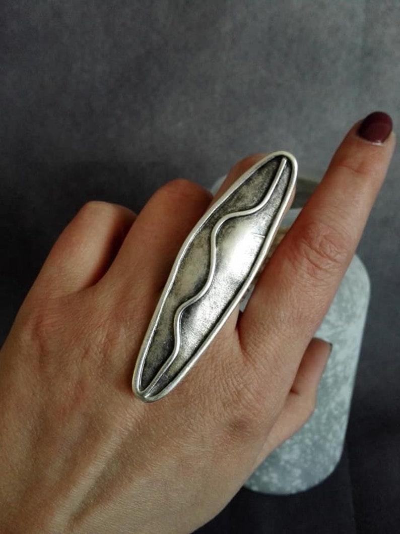 May include: A silver ring with a wavy design. The ring is oval shaped and has a textured finish.