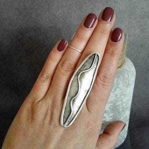 May include: A silver statement ring with a wavy design. The ring is oval shaped and has a textured finish.