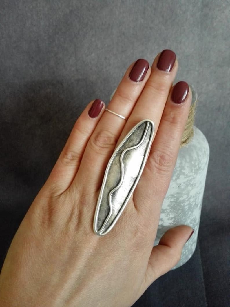 May include: A silver statement ring with a wavy design. The ring is oval shaped and has a textured finish.