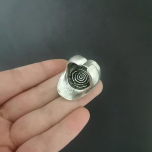 Puede incluir: Un anillo de plata con un dise&ntilde;o circular en espiral en el centro.