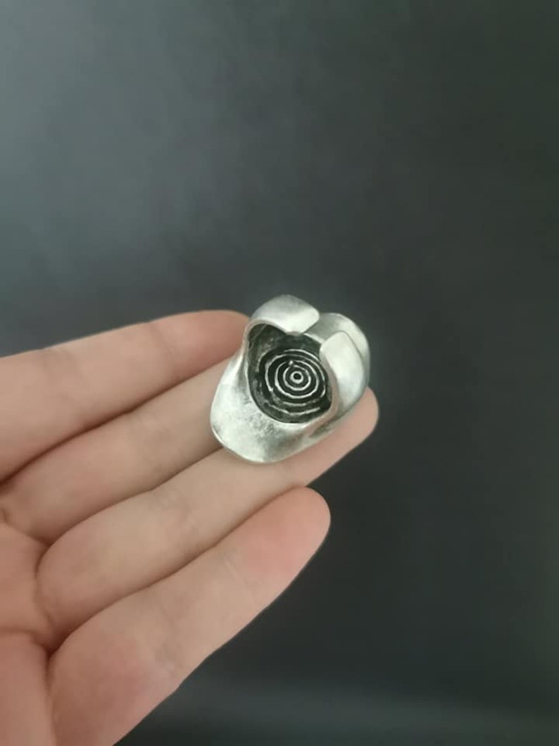Puede incluir: Un anillo de plata con un dise&ntilde;o circular en espiral en el centro.