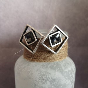May include: A pair of silver earrings with a square design and a black crystal in the center.