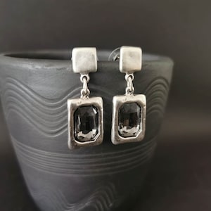 May include: A pair of silver dangle earrings with black rectangular stones. The earrings have a simple design and are perfect for everyday wear.